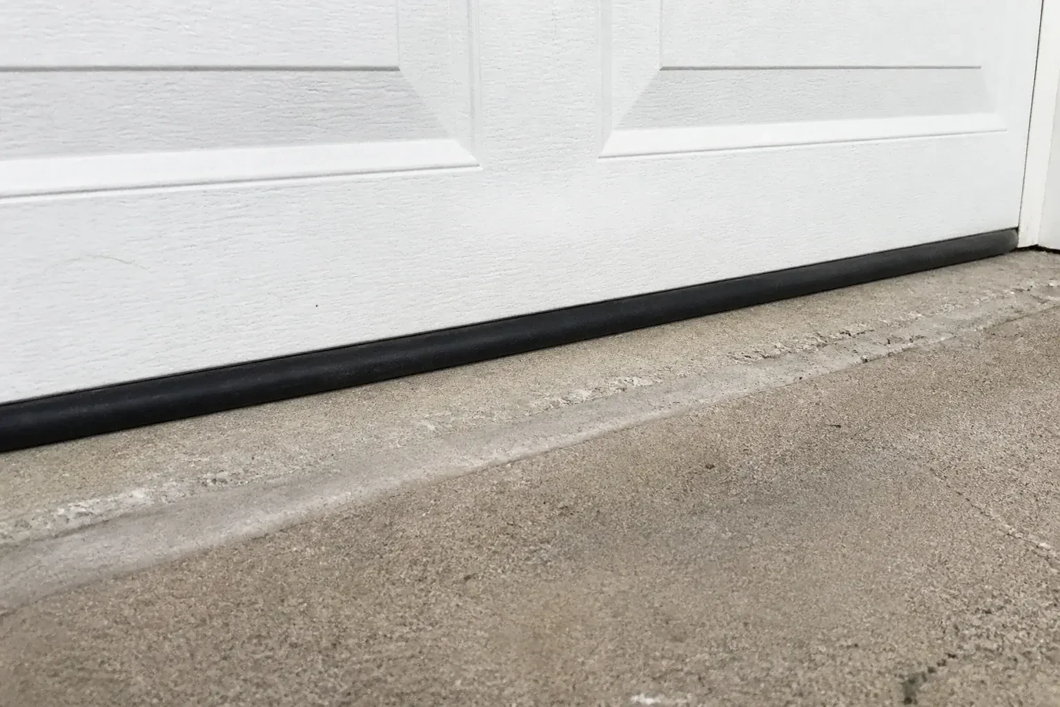 Black bottom seal along a closed white garage door at a concrete threshold. — Garage Door Bottom Seal Replacement, Toronto