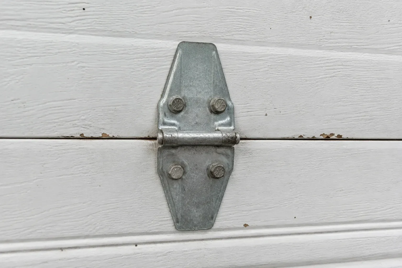 Metal center hinge across a seam in a white sectional garage door. — Garage Door Hinge Replacement, Toronto